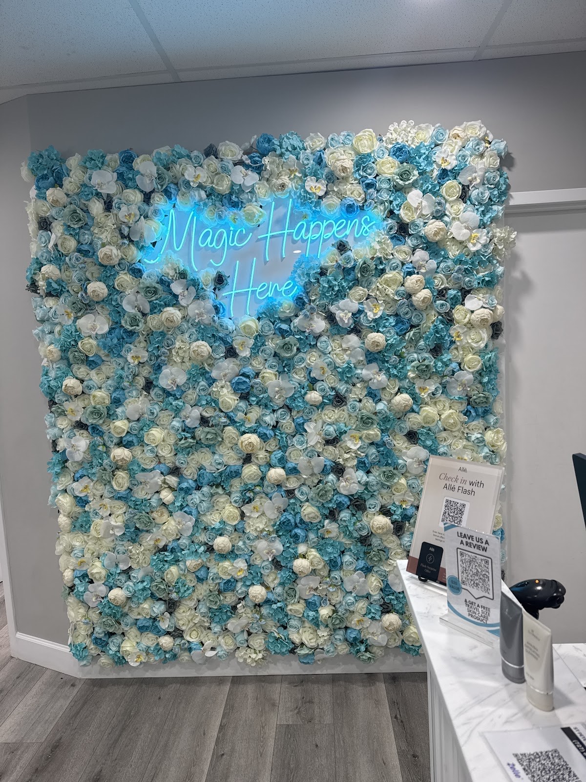 The spa's signature aqua, blue and white floral wall with a glowing 'Magic Happens Here' neon sign in the reception area
